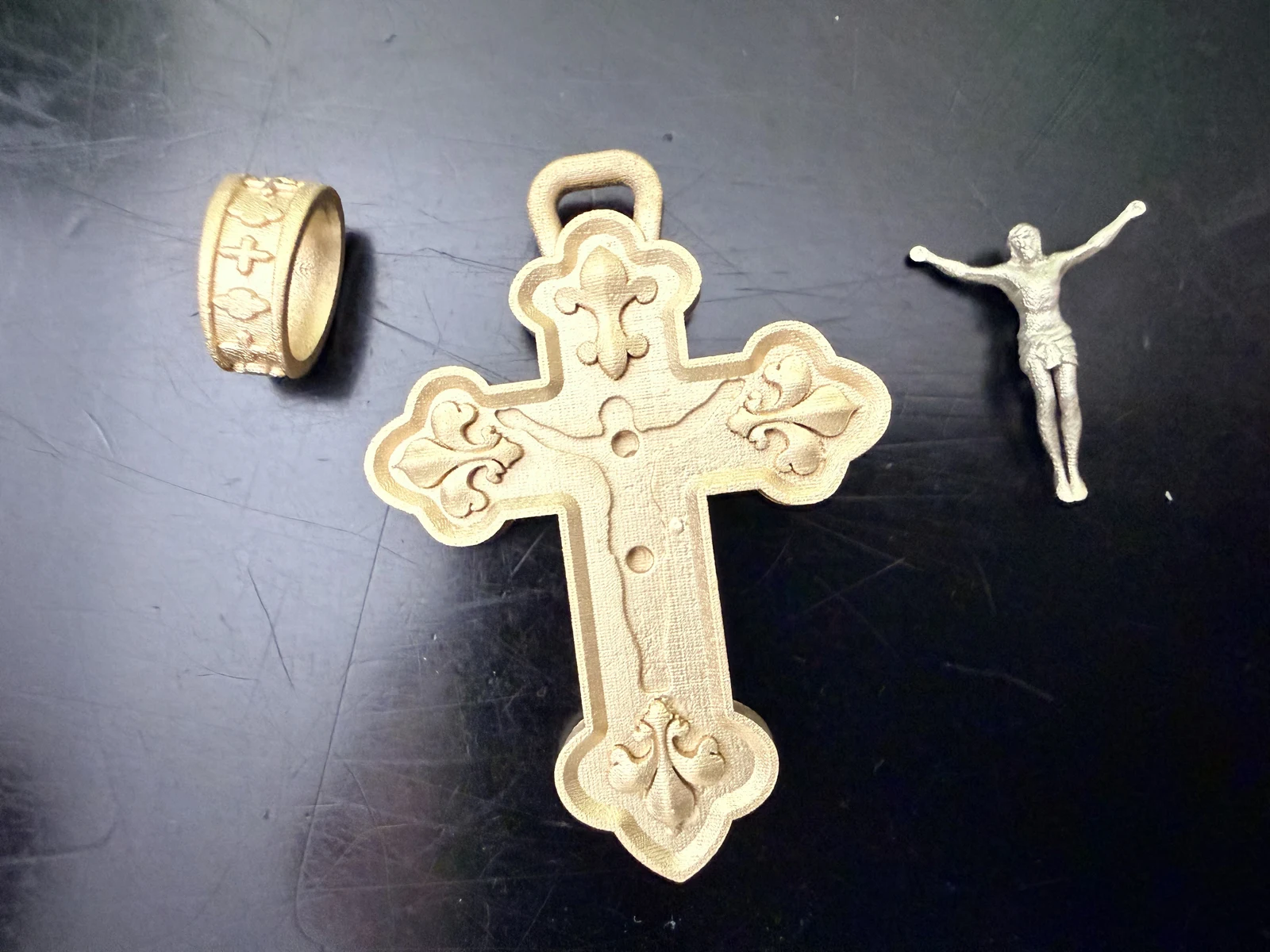 Raw gold cross and bail with separate white gold corpus on a dark surface