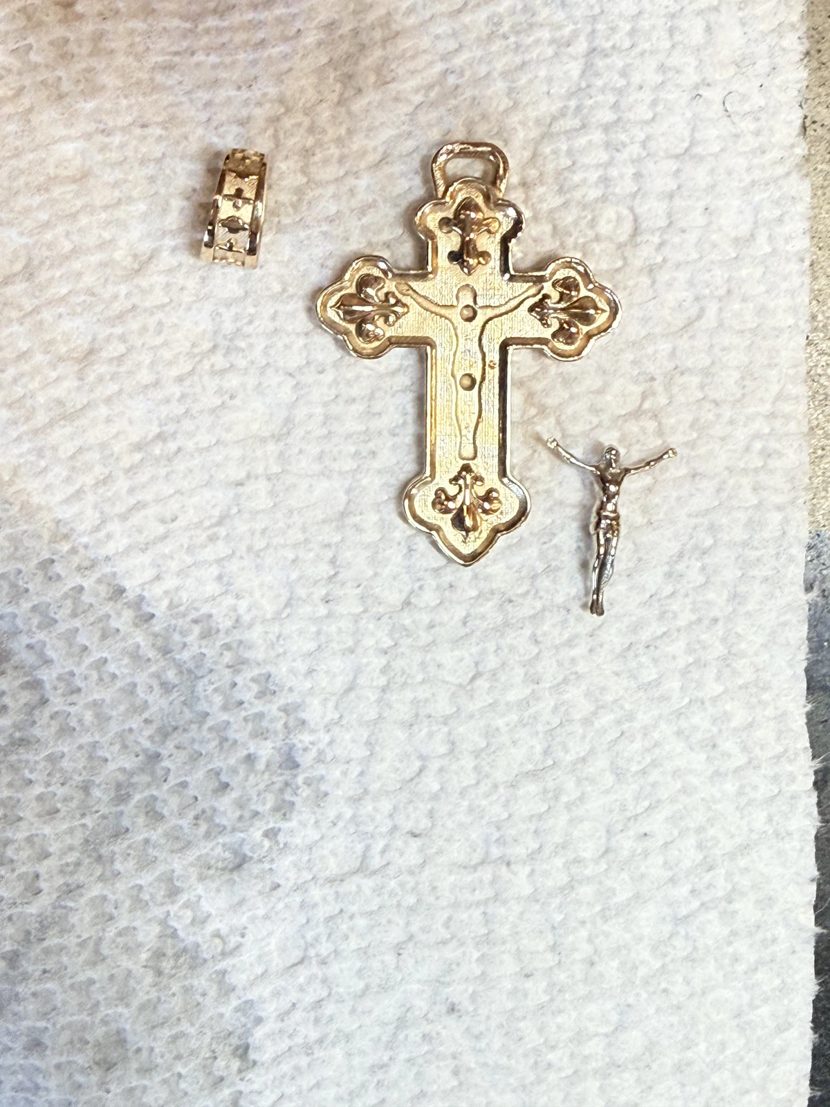 Pre-polished cross, bail, and corpus arranged separately on a white cloth