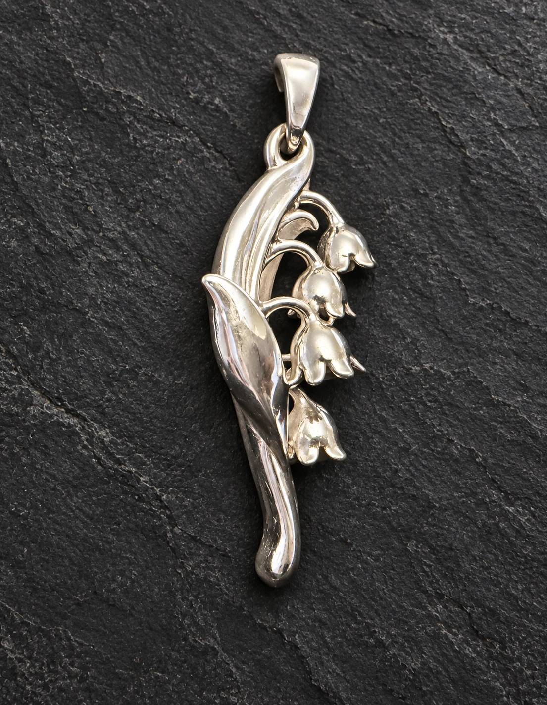 Lily of the Valley pendant with four bell-shaped flowers and a sweeping leaf on charcoal stone