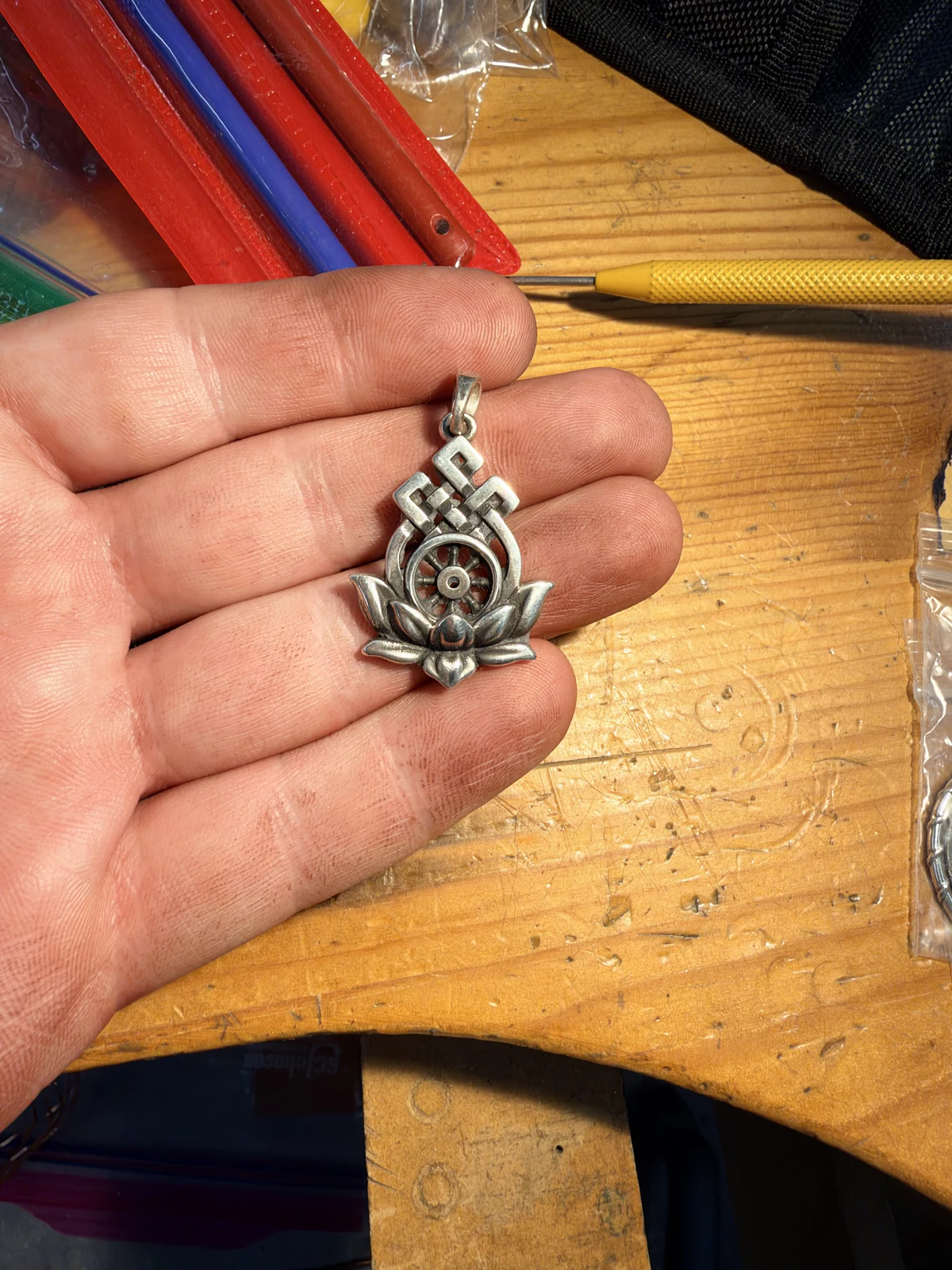 Oxidized silver lotus, Dharma wheel and endless-knot pendant held at the workbench